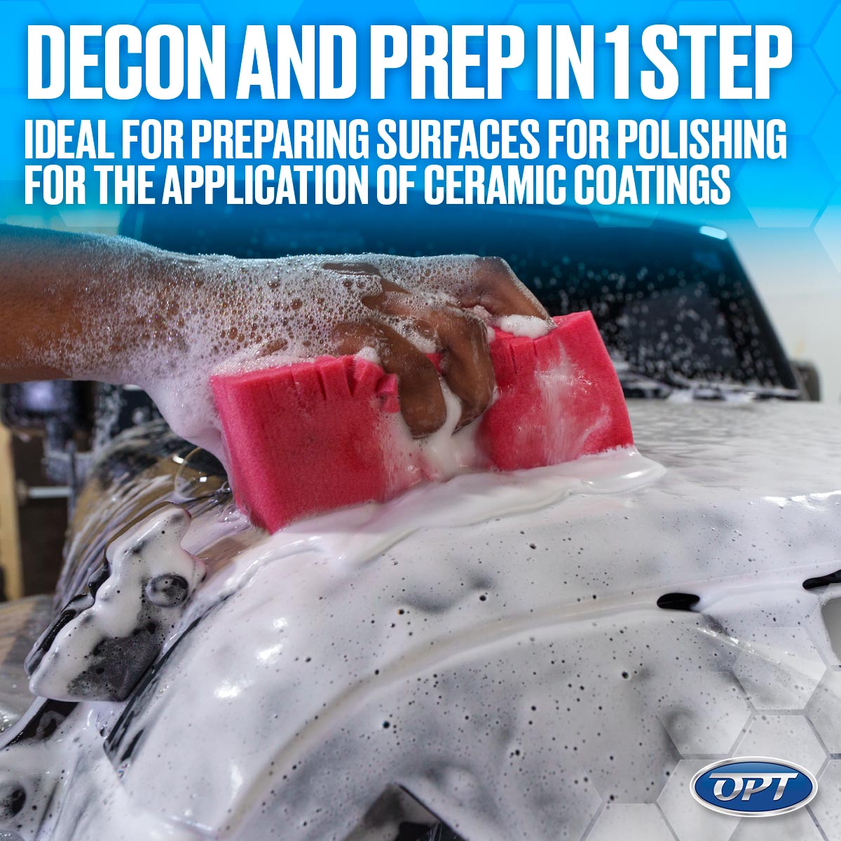A dark-skinned hand uses a bright pink sponge to apply thick white decontamination foam to a car's surface for ceramic coating preparation